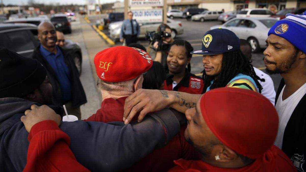 Secret Santa, in red Elf hat, gets hugs of thanks after handing out several $100 bills along West Florissant Avenue, Dec. 9, 2015, in Ferguson, Mo. Secret Santa is an anonymous Kansas City-area man who hands out cash to the needy during the holiday season and decided the Ferguson area is one place he wanted to stop this year.