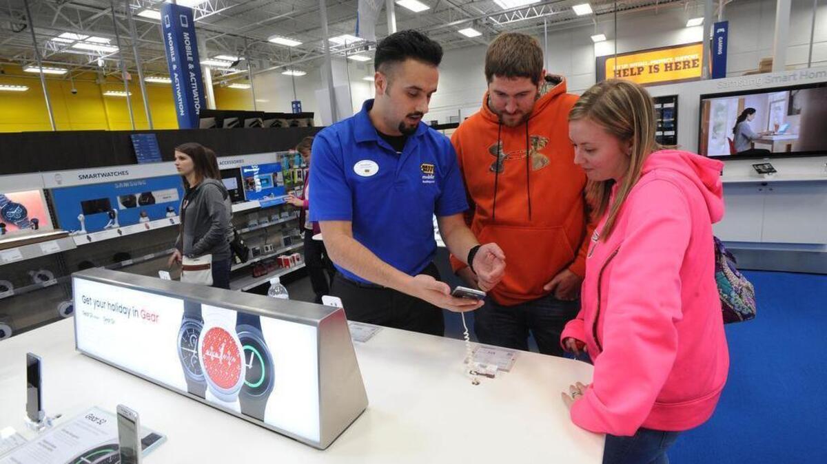 Best Buy mobile associate Jonathan Maust, left, shows a smart phone to customers Brad Oaks and his wife Nicole, of South Fork, Pa., on Nov. 27, 2015, in Johnstown, Pennsylvania. U.S. employers added 211,000 jobs in November, buoyed in part by strong gains in retail