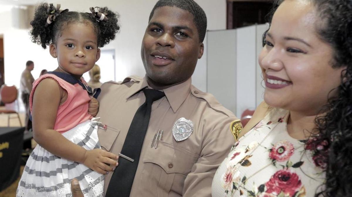 Andre Martin, center, holds his 2 year-old daughter Ariana as his finance Cynthia Mejia readies for a picture. Thursday morning, Andre Martin, a 26-year-old martial arts expert with a fiance and a child, was part of the new graduating class of Miami-Dade police.