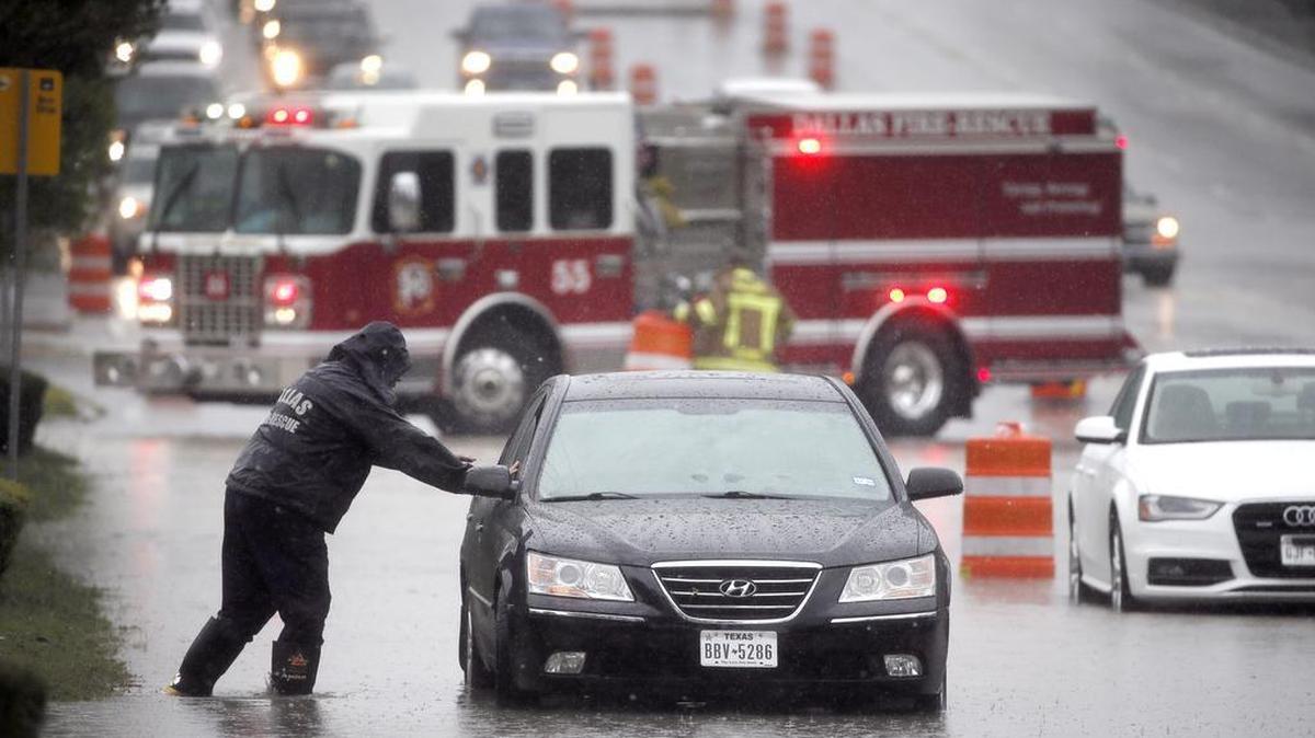 A Dalls Fire Rescue responder makes his way over to a stalled vehicle to check on the driver still inside on Friday in Dallas. The vehicle stalled after the road quickly flooded during a heavy rain fall.