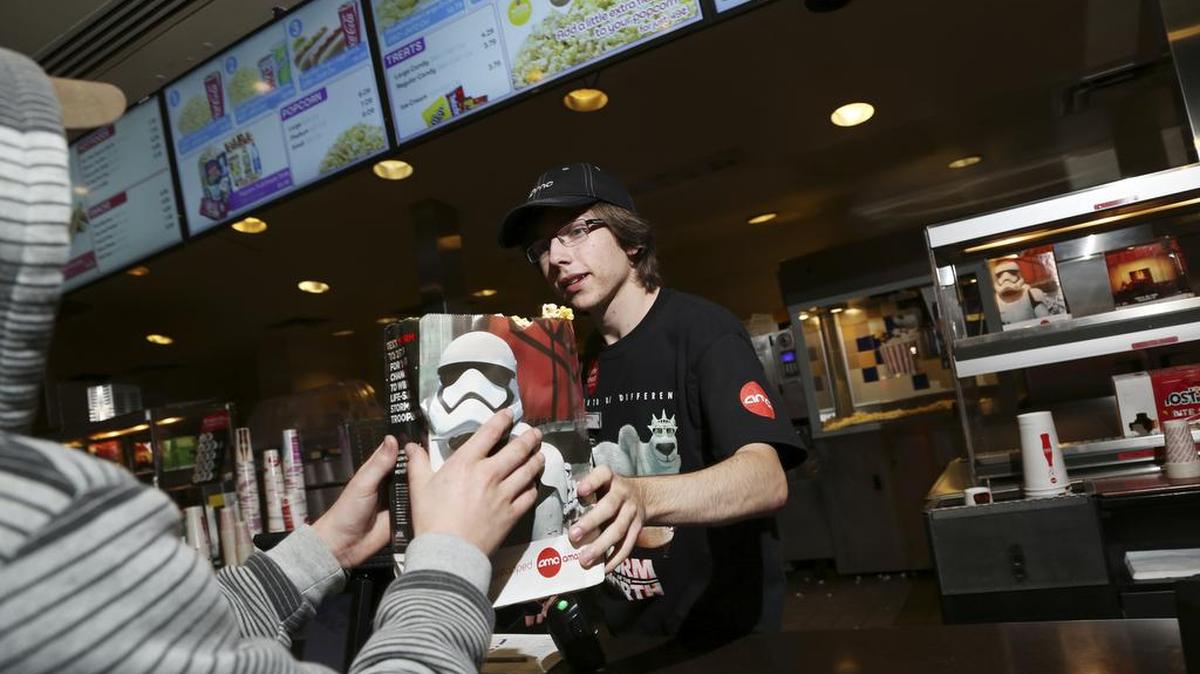 Henry Chandler hands popcorn to a customer Thursday at the AMC Barrywoods 24 in Kansas City, Mo. AMC Theaters and Regal Entertainment are rolling out technology that allows customers to preorder and prepay for food and soda from the comfort of their smartphones: The goal is to dramatically reduce time moviegoers spend waiting in line at the concession counter.