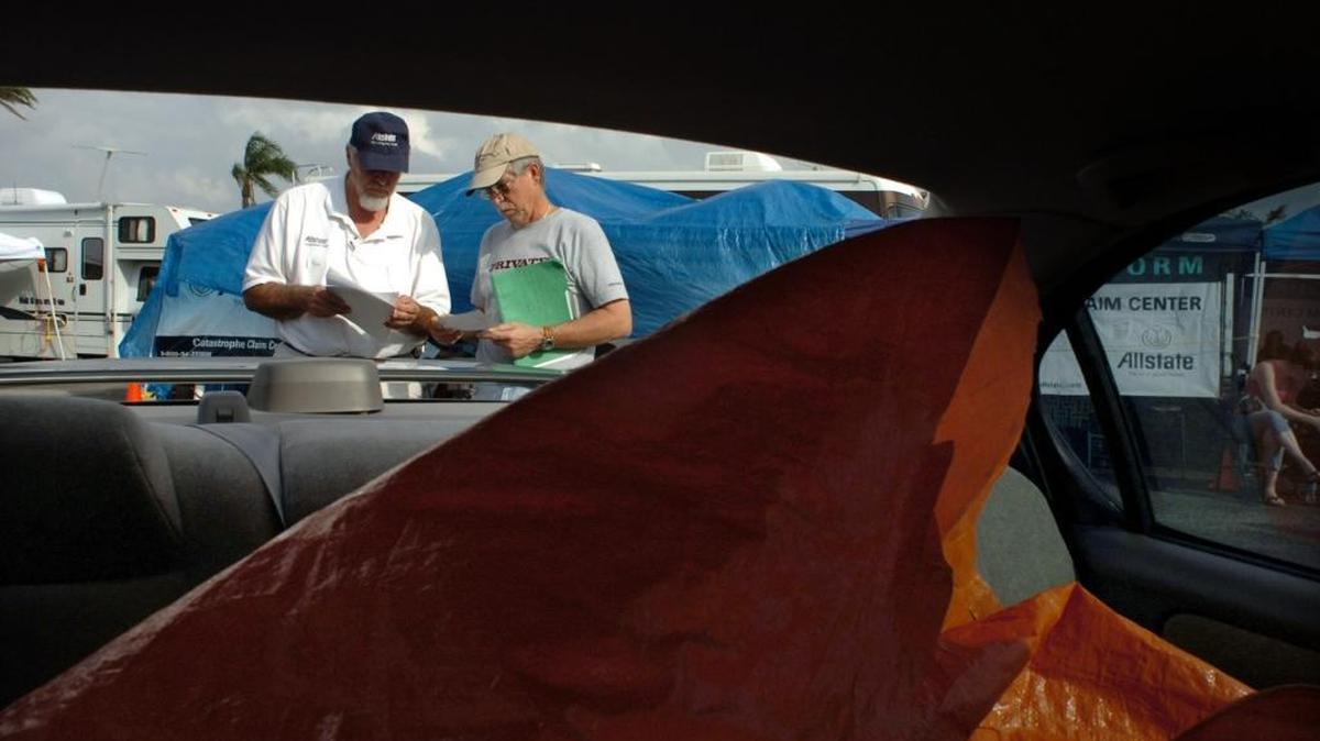 After Hurricane Wilma hit South Florida in 2005, Allstate insurance adjuster Robert Cartier, left, talked to Frank Miller of Hollywood, about his Nissan Maxima. A shed fell on the rear of his car knocking out the window and scratching the car. The photo shows a tarp peeled back to keep the rain from further damaging the car.