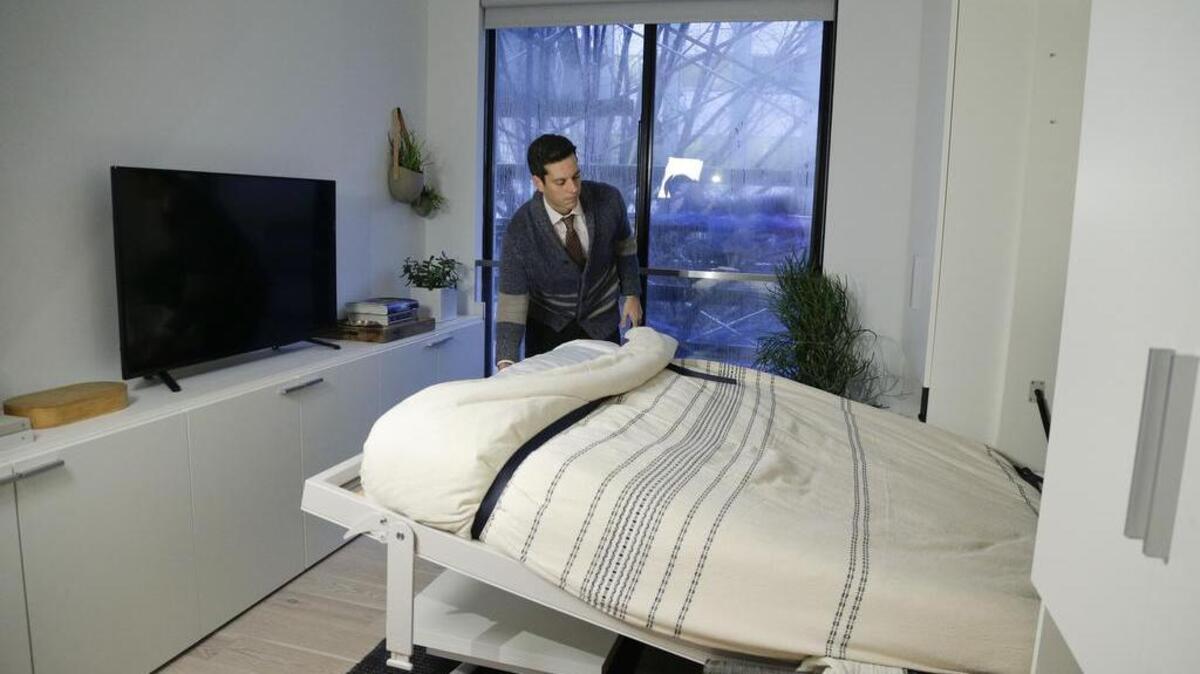 Stage 3 Properties co-founder Christopher Bledsoe demonstrates a retractable bed that turns into a sofa when stored inside one of the apartment units at the Carmel Place building in New York. As the city-sponsored “micro-apartment” project nears completion, it’s setting an example for tiny dwellings that the nation’s biggest city sees as an aid to easing its affordable housing crunch.