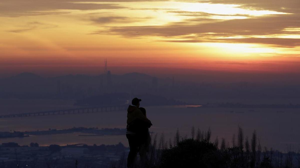A man and woman watch as the sun sets over the San Francisco skyline from Berkeley in December.