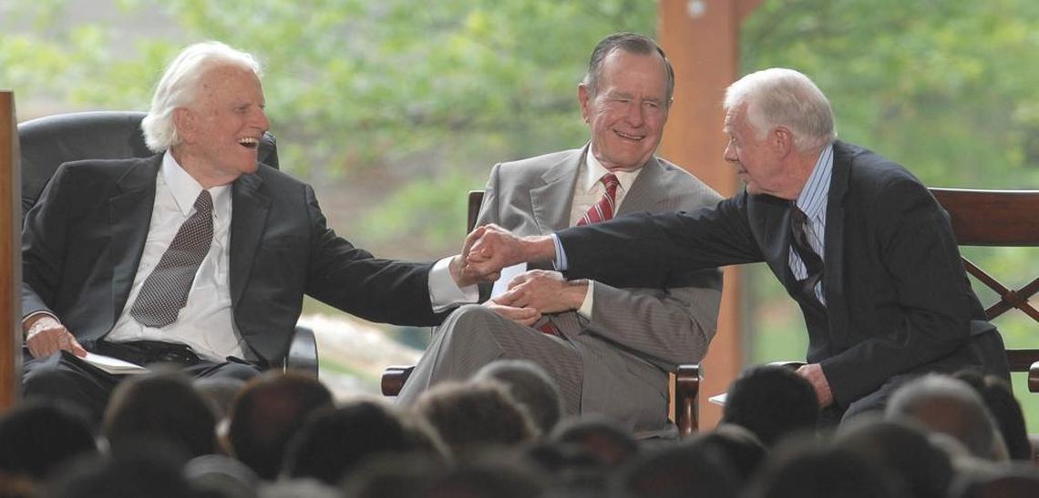 Billy Graham shakes hands with Jimmy Carter as George H.W. Bush looks on, at the Billy Graham Library in 2007.