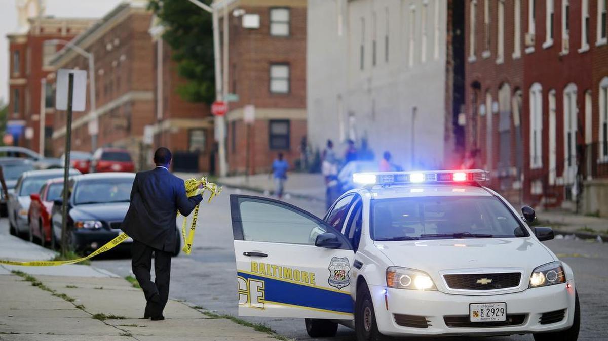 
In this July 30, 2015 picture, a member of the Baltimore Police Department removes crime scene tape from a corner where a victim of a shooting was discovered in Baltimore. Murders are spiking again in Baltimore, three months after Freddie Gray’s death in police custody sparked riots. 
