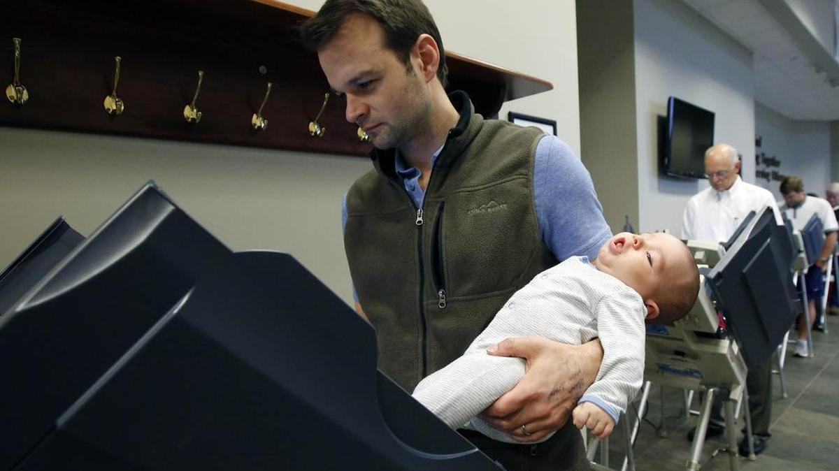 John Elliott takes advantage of the touchscreen voting booths to cast his ballot while holding his three-month-old son Dexter, Tuesday, Nov. 3, 2015, at a Ridgeland, Miss., precinct.