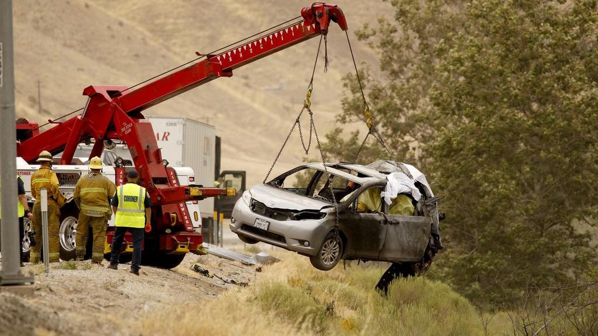 A tow truck lifts a burned minivan as investigators look over the scene of an accident on Tuesday, June 28, 2016 in Gorman, Calif. A semitrailer hit a minivan parked on the side of the highway and it burst into flames.