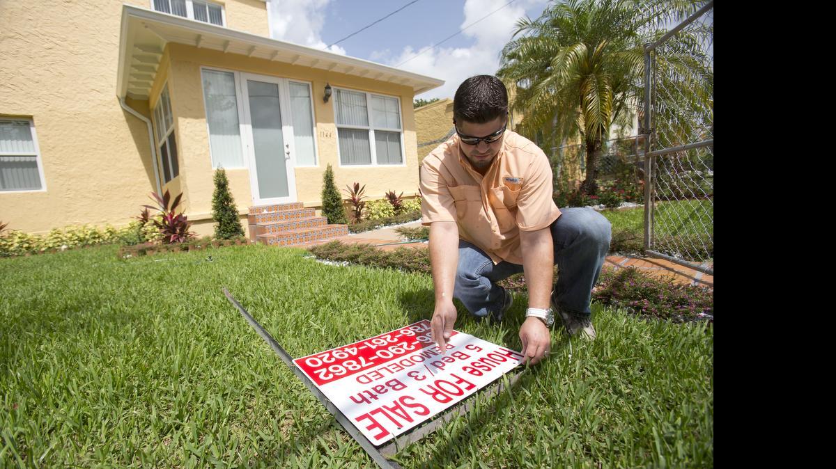 Robert Almirall, director of marketing and special assets coordinator for Mederos & Associates Real Estate Inc., prepares to put up a sign in front of a home in the Shenandoah neighborhood of Miami on April 24, 2015.