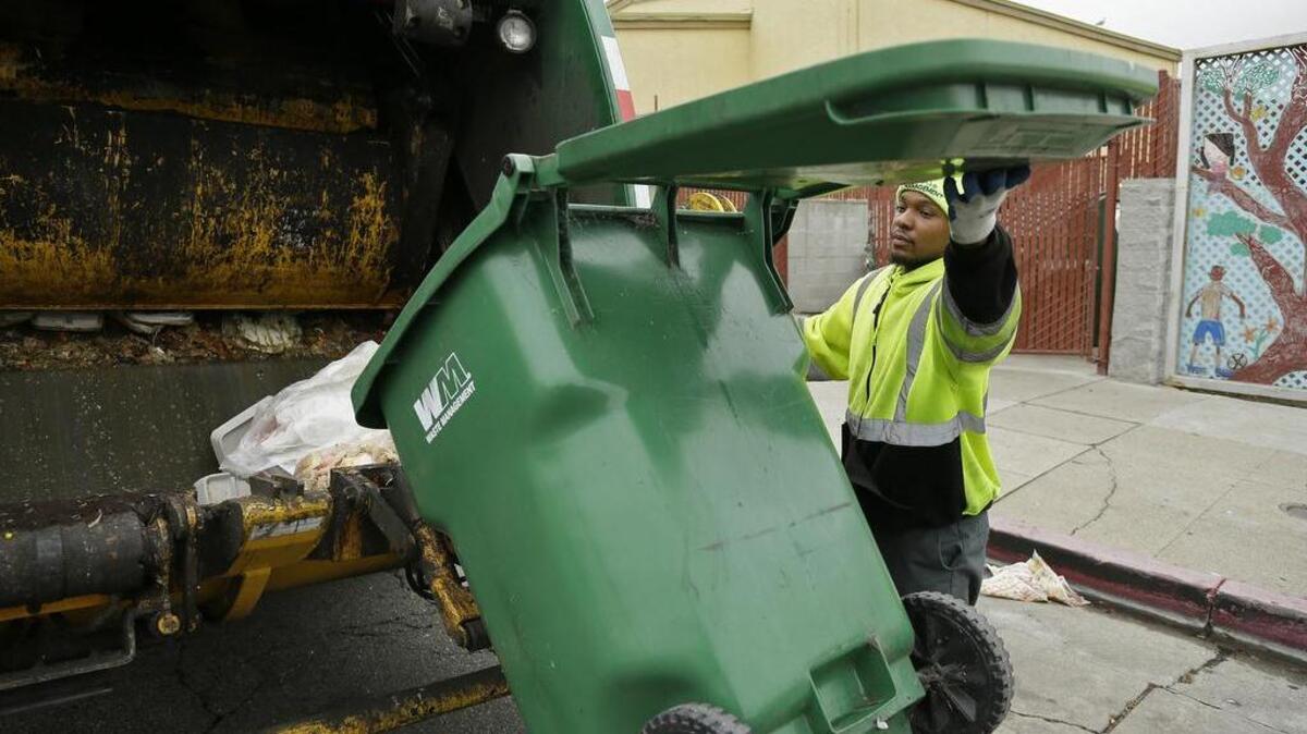 In this photo taken Thursday, Oct. 27, 2016, apprentice garbage man Corey Lever collects trash outside a school in Oakland, Calif. A new partnership between Waste Management of Alameda County Inc., the nonprofit Oakland Civicorps and unions gives young adults, often high school dropouts from low-income communities, a chance to become teamster drivers after two years of training.
