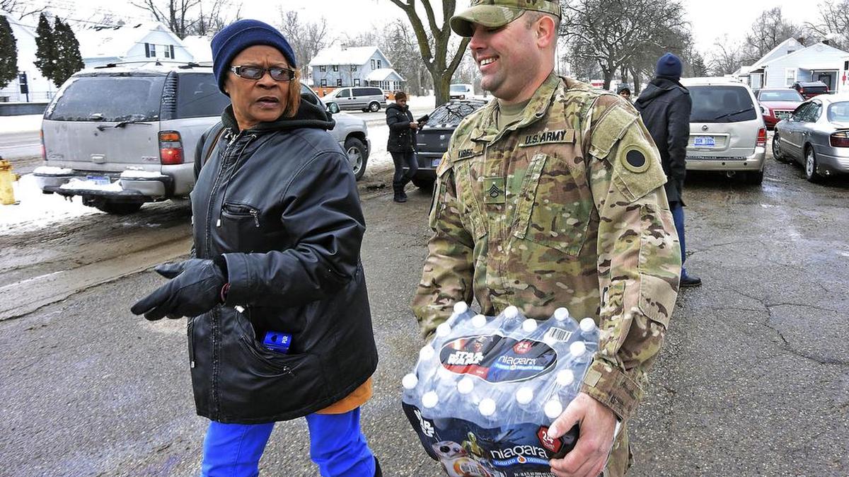Michigan National Guard Sgt. Steve Kiger of Harrison, Mich., carries water for a resident, Wednesday in Flint, Mich. Members of the Michigan National Guard began arriving in Flint on Wednesday for briefings on the drinking water crisis, ahead of a larger contingent of troopers who will help distribute bottled water, filters and other supplies to residents.