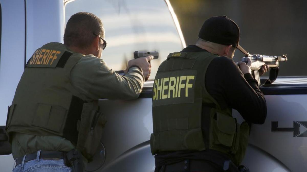 San Bernardino Sheriff’s deputies draw guns and take cover during an active search for the suspects involved in the mass shooting of 14 people at the Inland Regional Center in San Bernardino, Calif., on Wednesday, Dec. 2, 2015.