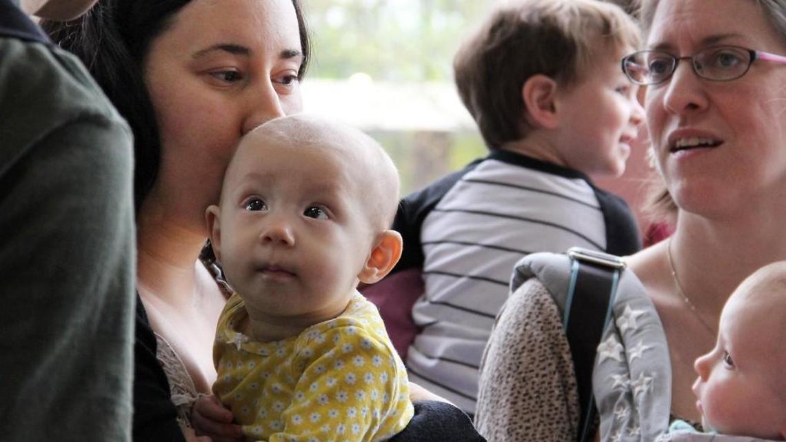 Evelyn Symes, 7 1/2 months, looks up at her father Jeff Symes from mother Yael Symes’ arms during a “nurse-in” Saturday at the Durham Costco on North Pointe Drive. About two dozen parents brought their babies to the warehouse store to show support for nursing mothers after Symes said she was made to feel uncomfortable while discretely breastfeeding Evelyn in the patio furniture department the day before.
