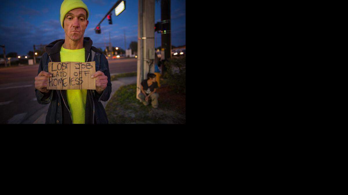 
Ryan Hoffman stands with a panhandling sign with his girlfriend, Michelle Pettigrew, in background, at a busy intersection in Lakeland, Fla., Jan. 7, 2015. Hoffman, once a 287-pound starting left tackle for the University of North Carolina football team, renowned for his toughness and durability, is now plagued with short-term memory problems and lives on the street, sometimes begging money from passing cars.
