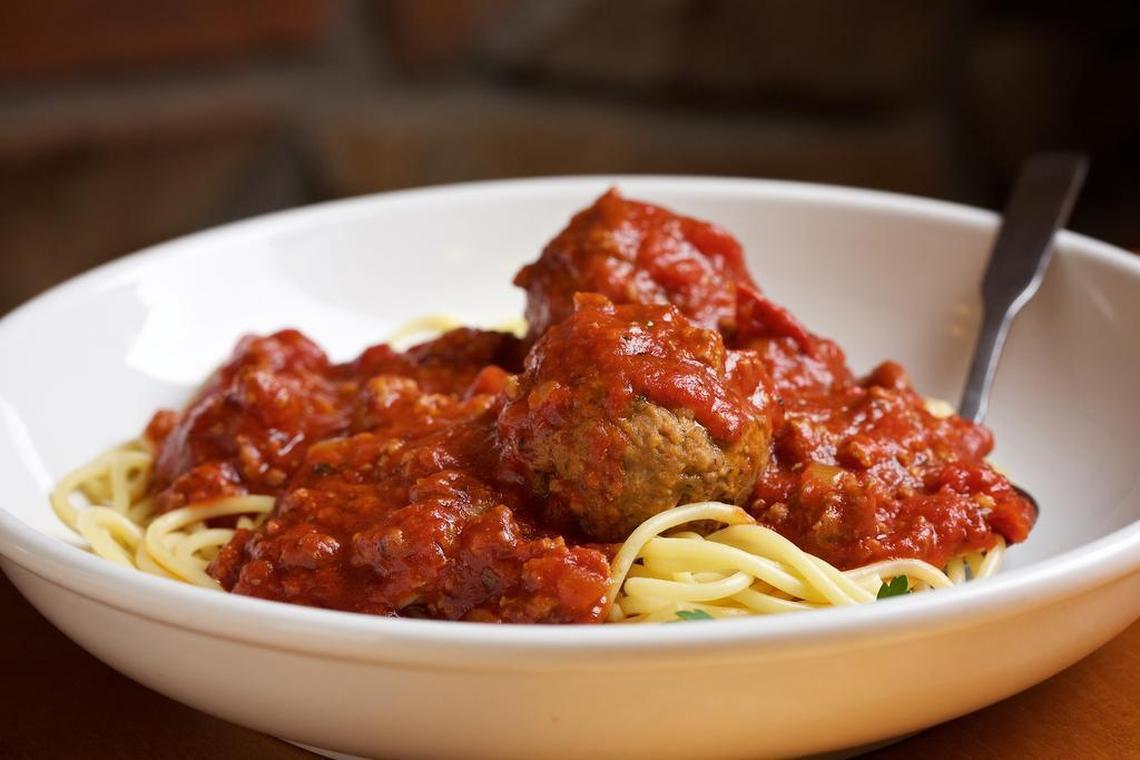 A close-up of a white bowl filled with spaghetti and a generous portion of meat sauce and large meatballs. A silver fork rests on the edge of the bowl.