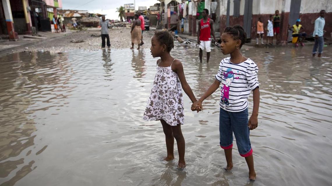 Two Haitian children, not eating tree bark, stand in a flooded street.