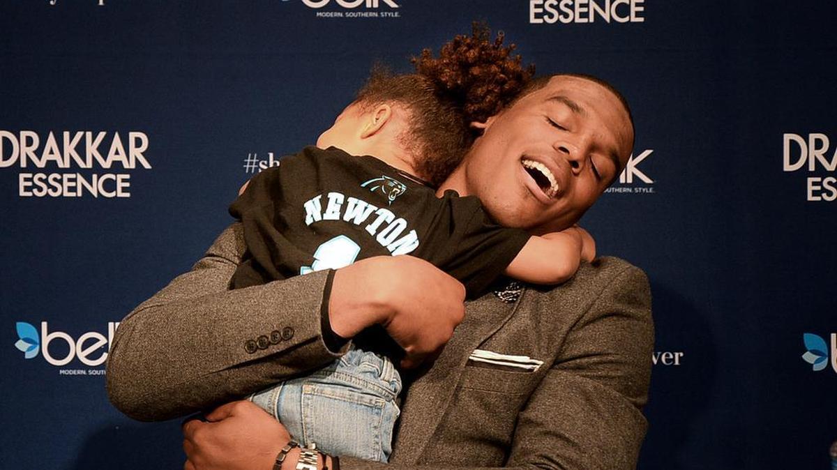 Cam Newton gets a big hug from Aubrie Lockhart, 3, in November 2014 as he signs bottles of Drakkar Essence for fans at Belk at SouthPark.