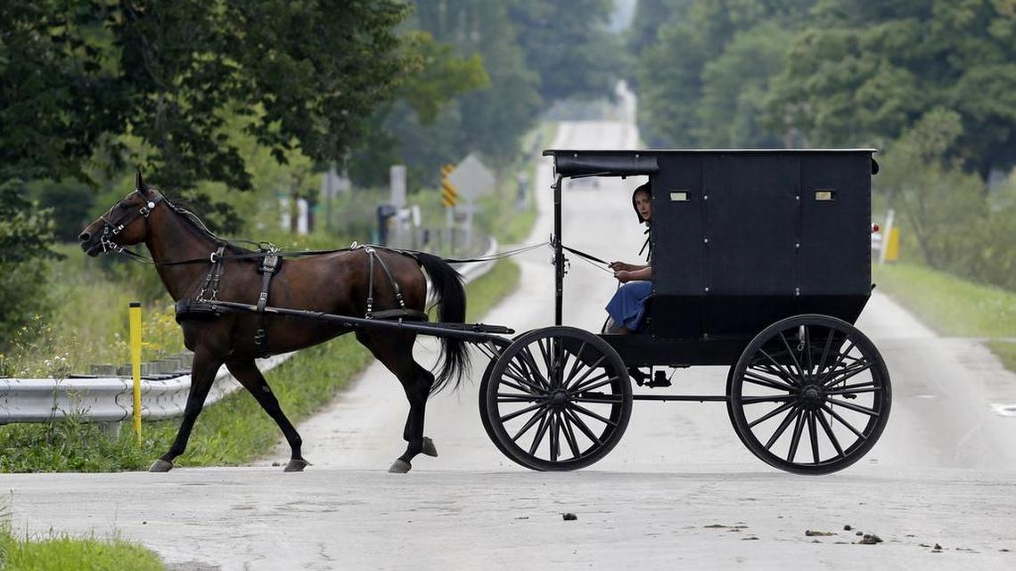 An Amish girl pears peers out from a buggy as it travels through an intersection in this Tuesday, Aug. 27, 2013, file photo from Middlefield, Ohio.