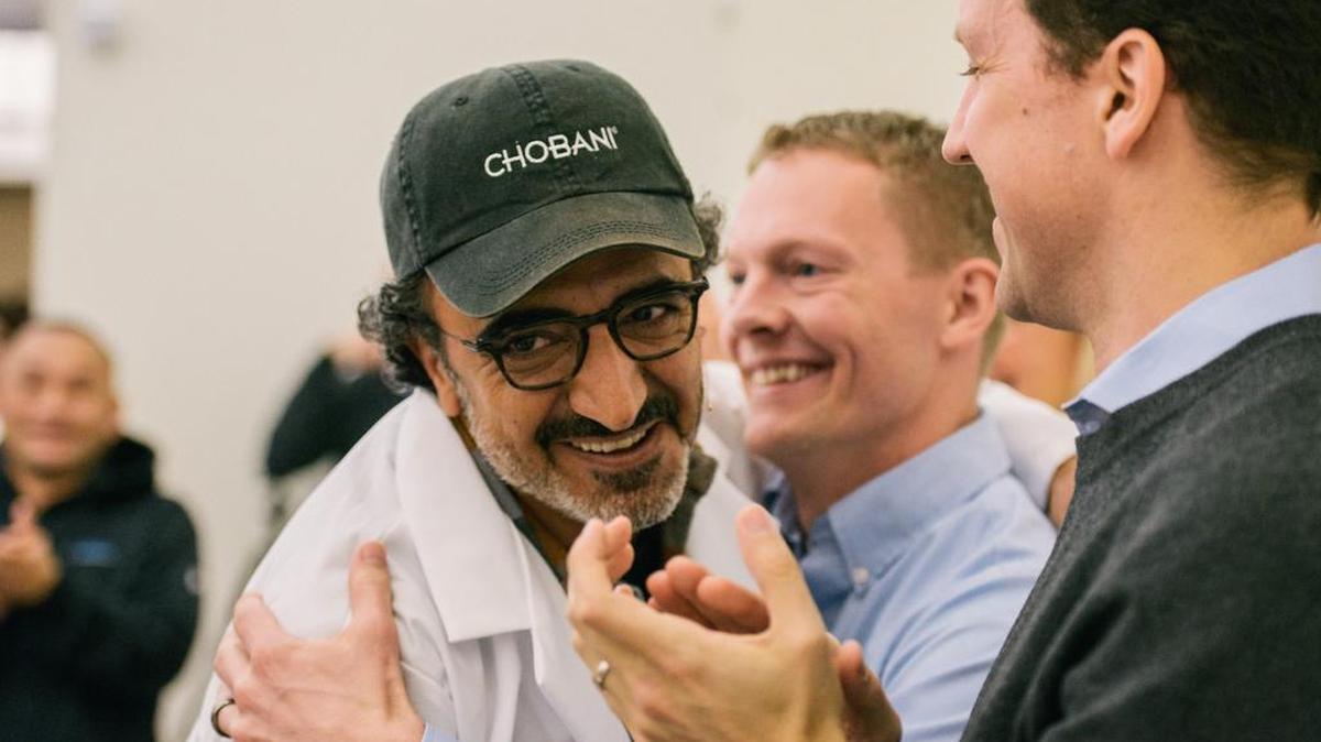 Employees hug Hamdi Ulukaya, left, a Turkish immigrant who founded the yogurt company Chobani in 2005. Ulukaya announced that he would give employees shares worth up to 10 percent of the company when it goes public or is sold.