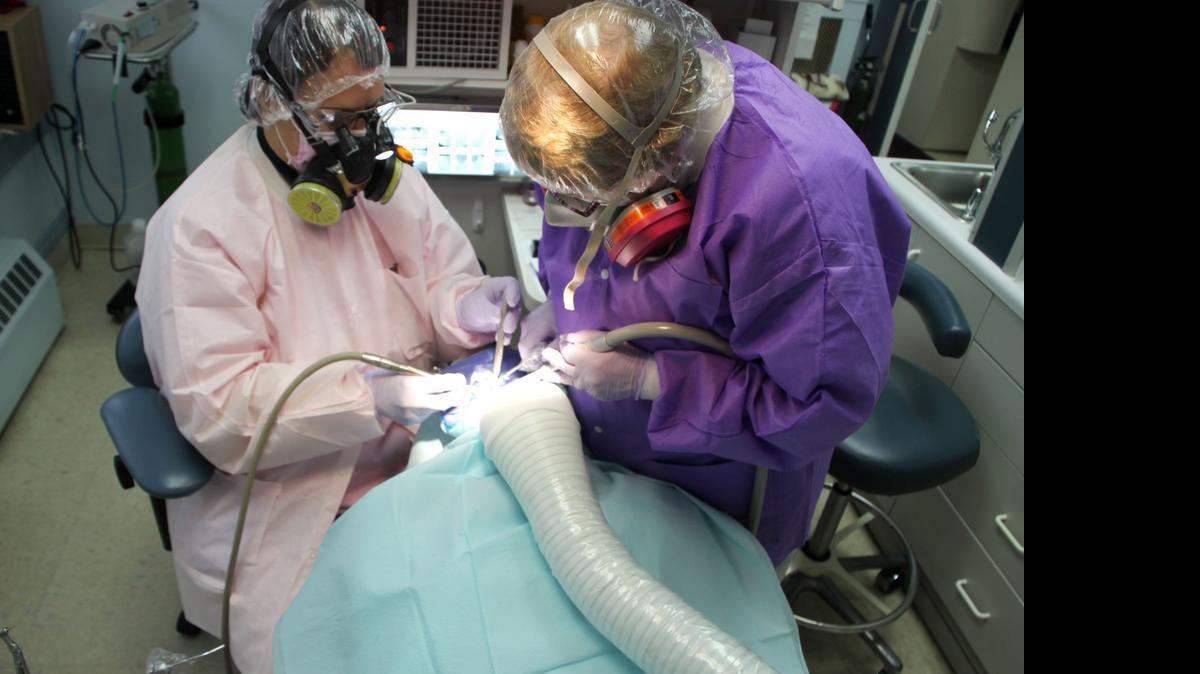 Scranton, Pa., mercury-free dentist Dr. Blanche Grube and her assistant remove a mercury/"silver filling" from a patient. All three are draped and covered for protection from mercury vapor and particles.