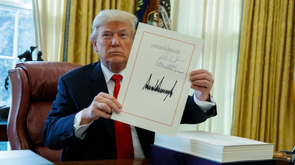 President Donald Trump shows off the tax bill after signing it in the Oval Office of the White House, Friday, Dec. 22, 2017, in Washington. The new law will create huge savings for utilities nationwide, but it is unclear the degree those regulated electric, gas and water companies will return savings to ratepayers.