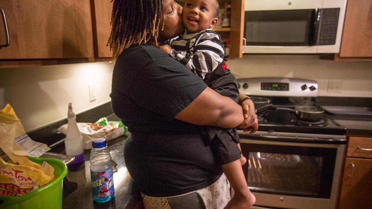 Gwen Wright, 22, holds her 1-year-old son, Amarion, while she makes food in her kitchen for a community Halloween party at Genesis, the subsidized apartment building where they live.