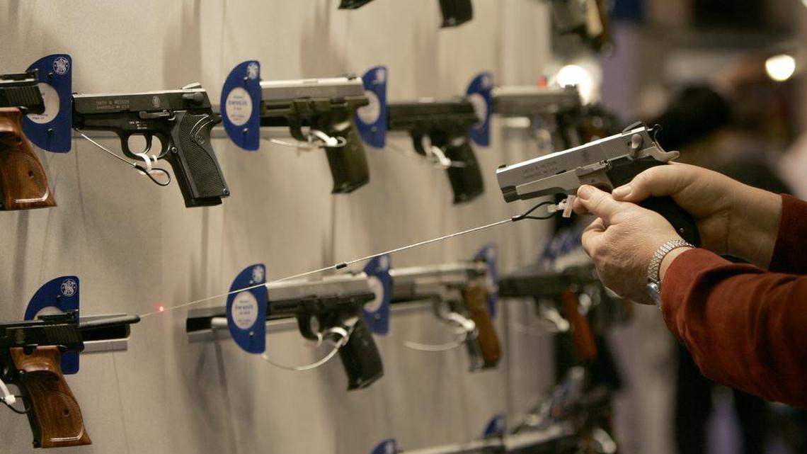 A woman points a handgun with a laser sight on a wall display of other guns during the National Rifle Association convention Friday, April 13, 2007, in St. Louis.