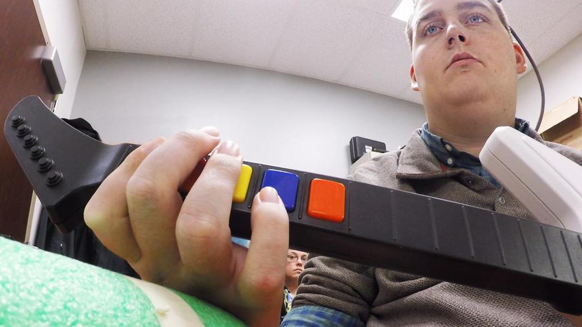 Ian Burkhart, 24, plays a guitar video game as part of a study with neural bypass technology. A computer chip in Burkhart’s brain reads his thoughts, decodes them, then sends signals to a sleeve on his arm that allows him to move his hand.
