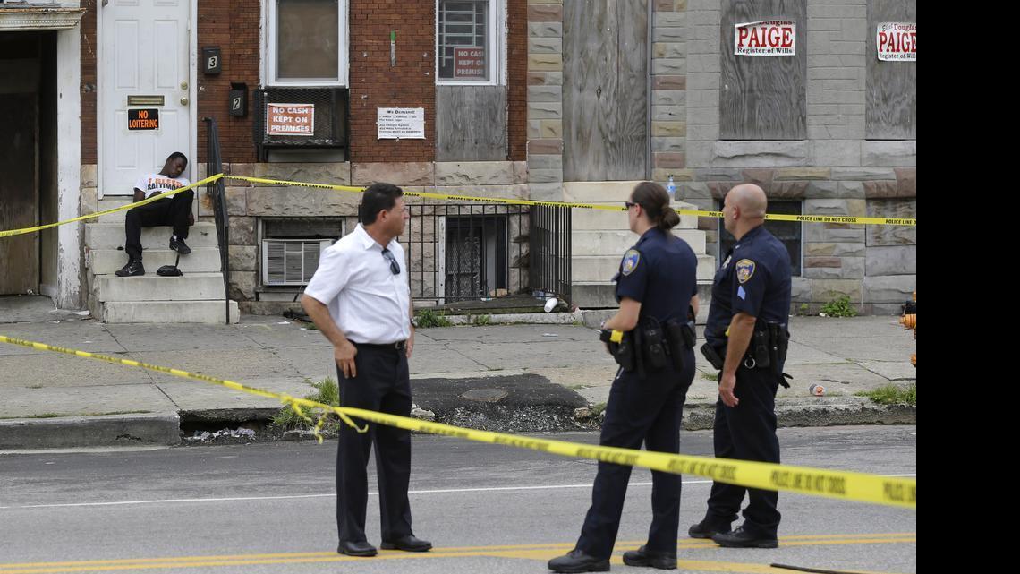 
A man sleeps on a stoop as police guard the perimeter of the scene of a shooting on Monday, July 27, 2015, in Baltimore. Police said a male was shot in the chest near the epicenter of unrest in April following the funeral of Freddie Gray. Rioting and looting broke out in the area after the funeral of Gray, a black man who suffered a fatal spinal cord injury in police custody. 
