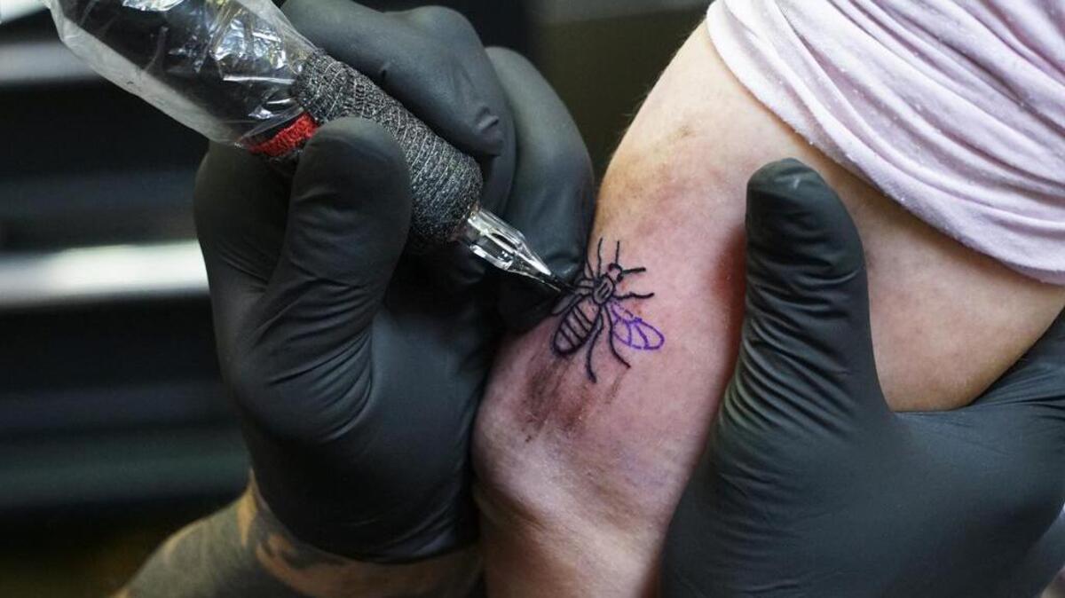 A tattoo artist tattoos a bee on a person's arm at his studio in Manchester, Sunday, May 28, 2017.