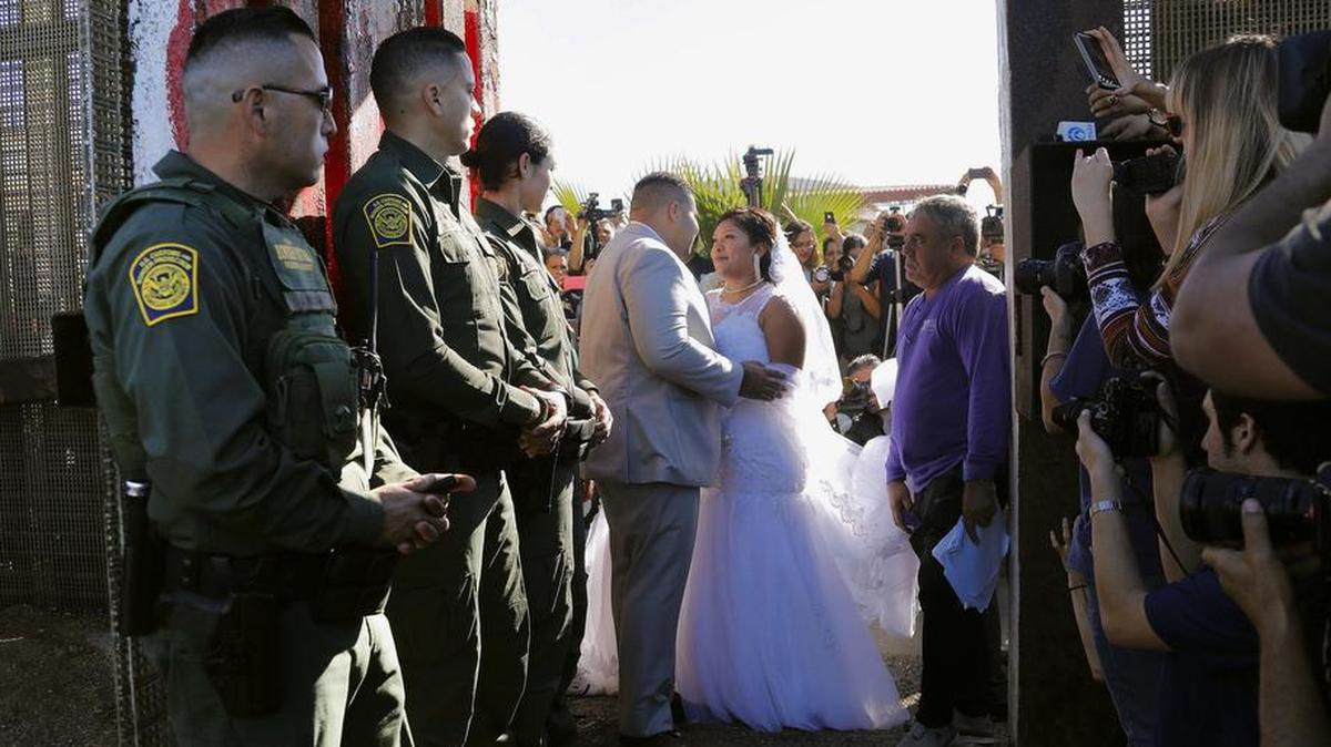 In this Nov. 18, 2017, photo, Brian Houston, of Rancho San Diego, center left, and Evelia Reyes, right, of Tijuana, Mexico, look at each other in their wedding at the "Door of Hope," part of the border fence between the U.S. and Mexico. A U.S. citizen, forbidden to enter Mexico, met and wed the love of his life in a brief moment when the gate separating the two countries was opened. Now it turns out the groom is a convicted drug smuggler and border agents are furious that he passed a federal background check and was approved for the "Door of Hope.”