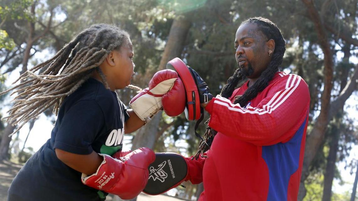 Kenneth Berry trains his son, Keing Berry, to box at MacArthur Park in Los Angeles, Sept. 14, 2016. Berry was was shot three times decades ago, but is still in pain and has to walk with a cane. The expansion of state Medicaid programs under the health care law has brought coverage, and necessary treatment, to previously uninsured shooting victims.