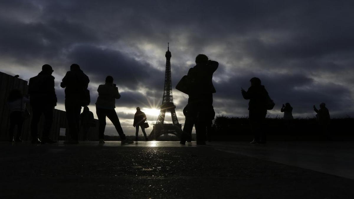 Tourists visit the site of Eiffel Tower which remained closed on the first of three days of national mourning in Paris, Sunday, Nov. 15, 2015. Thousands of French troops deployed around Paris on Sunday and tourist sites stood shuttered in one of the most visited cities on Earth while investigators questioned the relatives of a suspected suicide bomber involved in the country's deadliest violence since World War II.