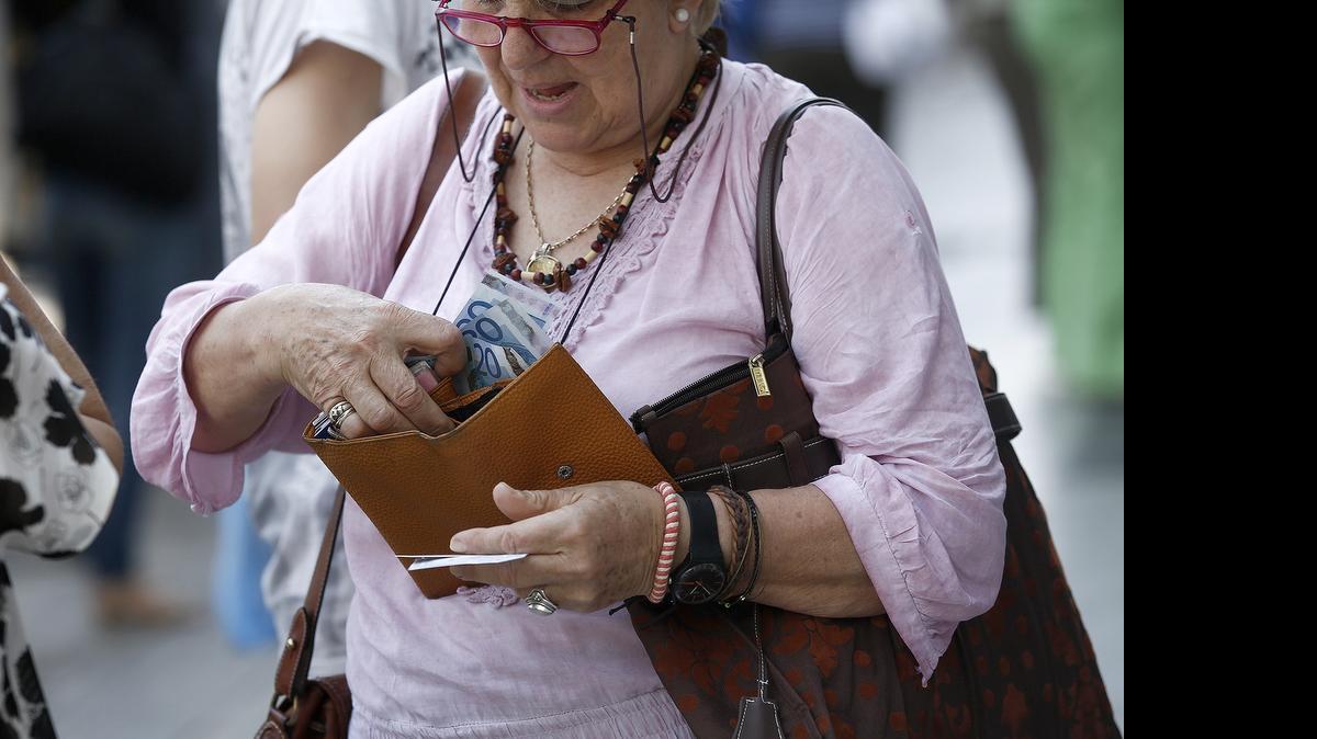 
A customer places her daily cash machine withdrawal limit of 60 euros into her purse after using an automated teller machine outside a closed Eurobank Ergasias bank branch in Athens on Monday.
