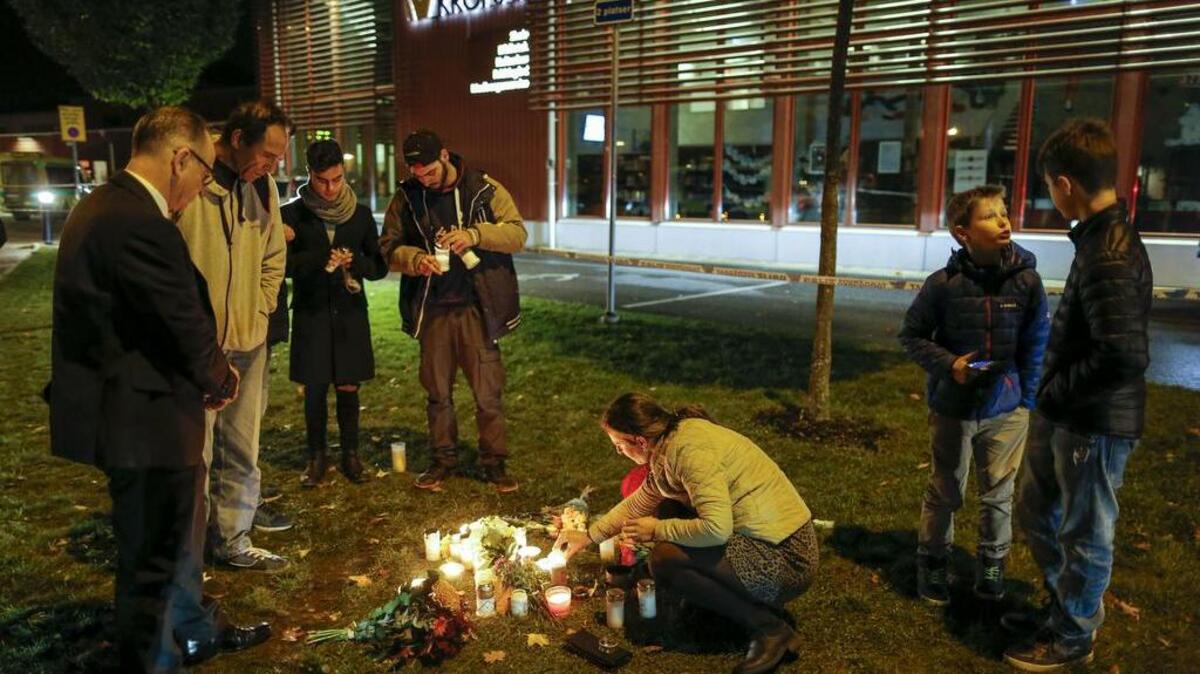 People light candles and lay flower tributes outside the school Thursday afternoon where a masked man stabbed four people Thursday Oct. 22, 2015, in Trollhättan, Sweden, killing two before he was shot to death.