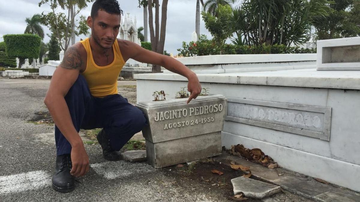 Yossel García, a gravedigger at Havana's famed Colon Cemetery, points to the back of a marble planter at the tomb of prominent banker Jacinto Pedroso. To uncover the name, Garcia had turned the planter around – the name had been placed to the back. Pedroso’s name on the mausoleum itself, at right, has been obscured with a puttylike substance.
