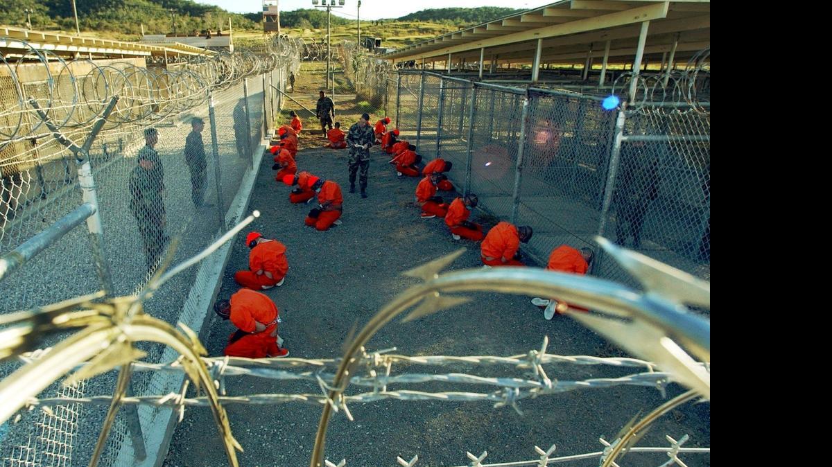 
In this handout photo from the Department of Defense, Taliban and al-Qaida detainees in orange jumpsuits sit in a holding area watched by military police at Camp X-Ray at Naval Base Guantanamo Bay, Cuba, during in-processing to the temporary detention facility on Jan. 11, 2002. 

