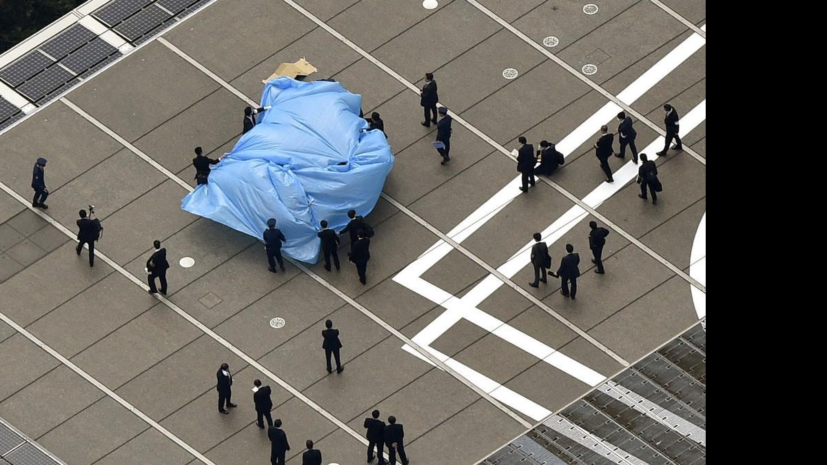 
Investigators gather around a small drone covered with blue sheets, on the roof of Prime Minister Shizo Abe's official residence in Tokyo Wednesday, April 22, 2015. Japanese authorities were investigating Wednesday after the small drone reportedly containing traces of radiation was found on the roof of the prime minister's office, sparking concerns about drones and their possible use for terrorist attacks.
