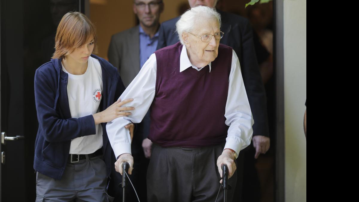 
With the help of a Red Cross worker, former SS guard Oskar Groening leaves the court after the verdict of his trial in Lueneburg, Germany, Wednesday, July 15, 2015. Groening, 94, who served at the Auschwitz death camp was convicted on 300,000 counts of accessory to murder and given a four-year sentence. 
