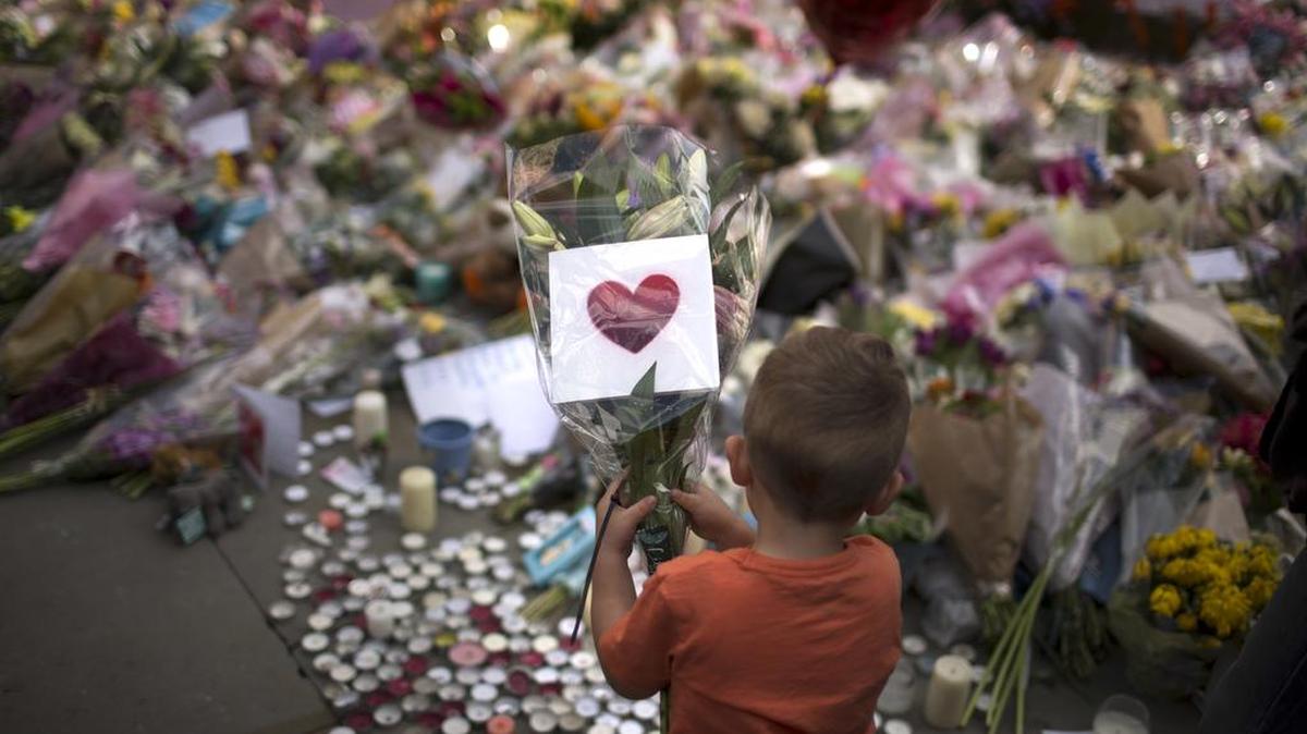 A child places flowers in a square in central Manchester, Britain, Wednesday, May 24, 2017, after the suicide attack at an Ariana Grande concert that left more than 20 people dead and many more injured on Monday night at the Manchester Arena.