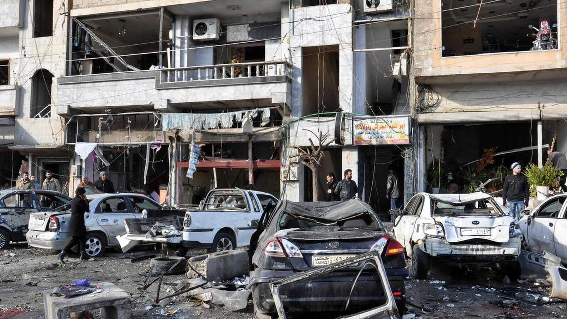 In this photo released by the Syrian official news agency SANA, Syrian citizens gather at the scene where twin bombs exploded at a government-run security checkpoint, at the neighborhood of Zahraa, in Homs province, Syria, Tuesday, Jan. 26, 2016.