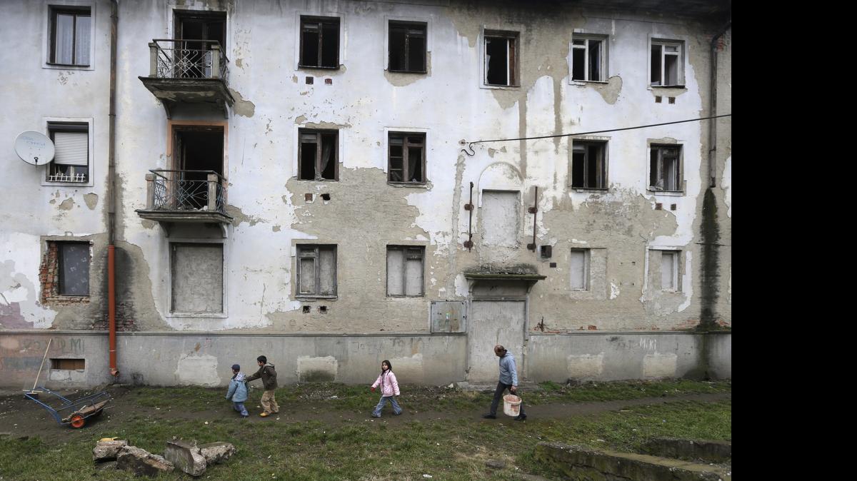 
In this March 2, 2015 photo, residents walk past their house in a Roma settlement in Kralovsky Chlmec, Slovakia. Each year, dozens of women from the poorer corners of eastern Europe are lured to travel to western Europe for sham marriages with men who pay large sums because they want to live, work or claim benefits more easily in their chosen country and move freely within Europe. 
