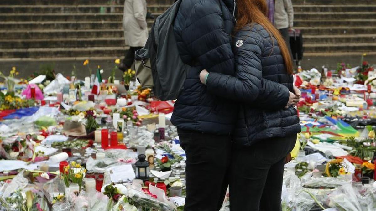 A couple embrace in front of tributes placed in a memorial for victims of the recent attacks on Brussels at the Place de la Bourse on Friday, March, 25, 2016. Amid signs that life in Brussels was returning to some sort of normality on the third day of mourning the dead, authorities lowered Belgium’s terror-threat level by one notch. However, they said the situation remained grave and another attack is “likely and possible.” Belgium had been on its highest alert since Tuesday’s bombings.
