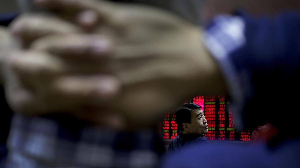 A man chats with other investors near an electronic board displaying stock prices at a brokerage house in Beijing, Tuesday, Jan. 19, 2016.