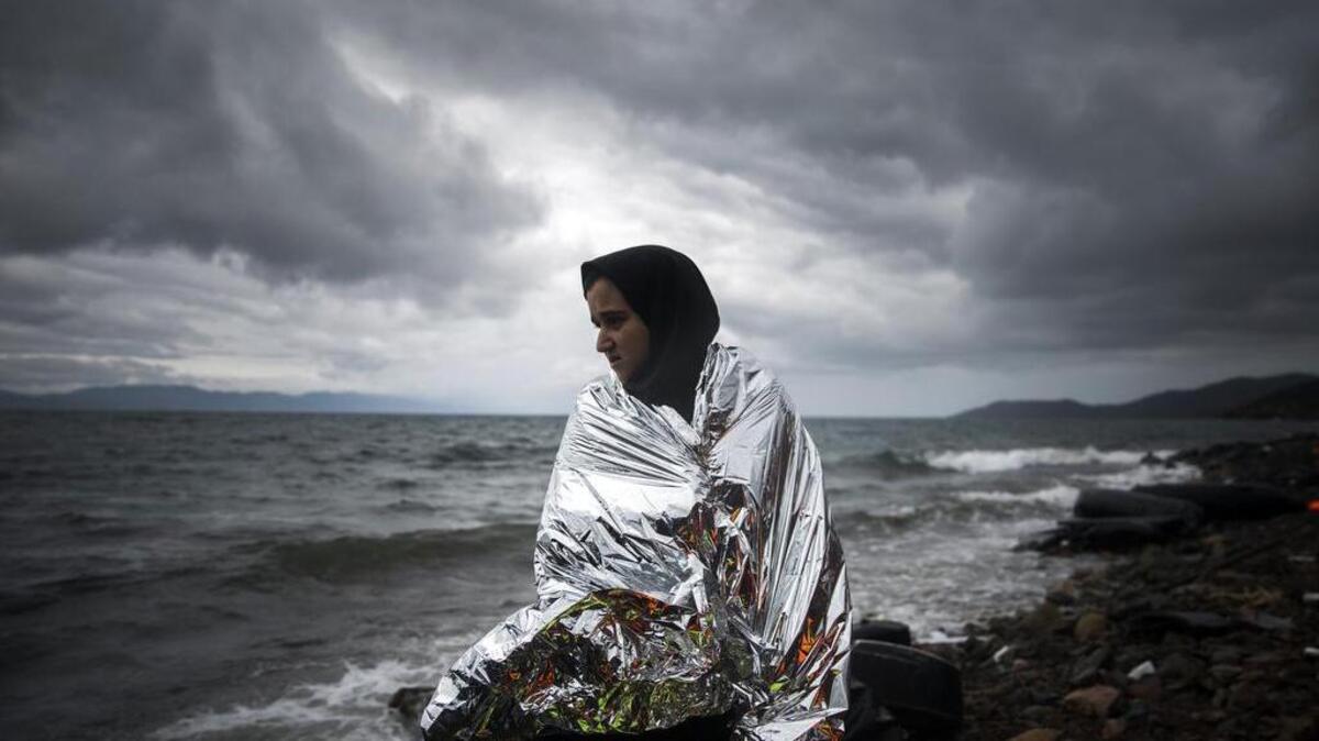 A woman tries to warm up herself using a thermal blanket provided by volunteers after arriving on a dinghy from a Turkish coast to the northeastern Greek island of Lesbos on Saturday. The International Office for Migration says Greece over the last week experienced the largest single weekly influx of migrants and refugees this year, at an average of some 9,600 per day.