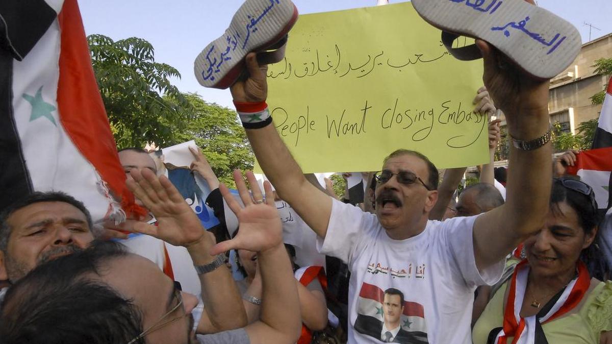 
Hundreds of thousands of Syrians protest in front the U.S. Embassy in Damascus against the visit of the U.S. Ambassador to Syria, Robert Ford, who visited the city of Hama, Syria, on July 7, 2011. The Arabic words on the shoes read: "The dirty ambassador," right, and "the U.S. ambassador," left.

