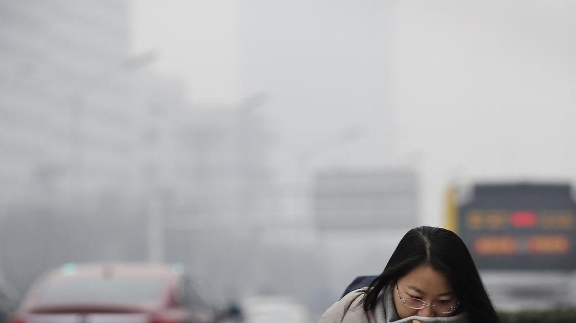 A woman uses a scarf to cover her face from pollutants as she walks out of an underpass tunnel on a polluted day in Beijing on Tuesday. Schools closed and rush-hour roads were much quieter than normal as Beijing’s first-ever red alert for smog took effect Tuesday, closing many factories and invoking restrictions to keep half the city’s vehicles off the roads.