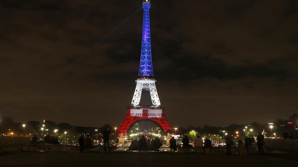 People look at the Eiffel Tower illuminated in the French colors in honor of the victims of the attacks on Friday in Paris, Monday, Nov. 16, 2015. France is urging its European partners to move swiftly to boost intelligence sharing, fight arms trafficking and terror financing, and strengthen border security in the wake of the Paris attacks.
