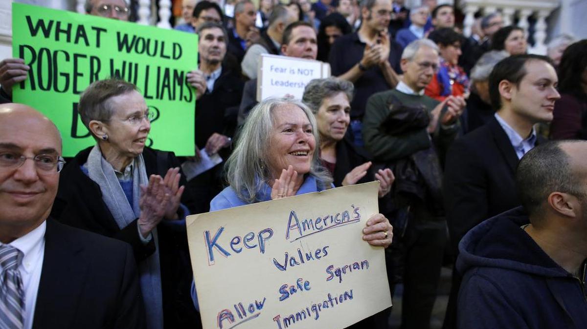 Linda Kushner, of Providence, R.I., center, displays a placard during a rally Thursday, Nov. 19, 2015, at the statehouse in Providence, demanding that Syrian refugees be allowed to enter Rhode Island and the United States following the terror attacks in Paris.
