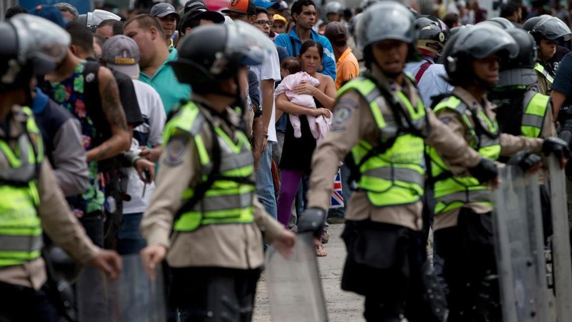 A woman holding a baby looks at police in riot gear standing guard as she and others wait outside a supermarket to buy food in Caracas, Venezuela in this June 1, 2016 file photo. A new Gallup polls found that citizens in Venezuela feel less safe in their country than citizens in Syria.